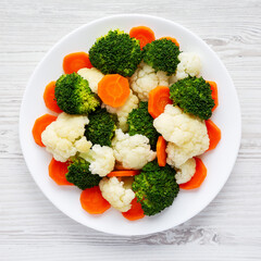 Mixed Organic Steamed Vegetables (Carrots, Broccoli and Cauliflower) on a Plate on a white wooden background, top view. Flat lay, overhead, from above.