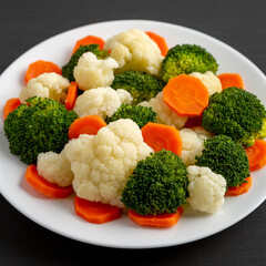 Mixed Organic Steamed Vegetables (Carrots, Broccoli and Cauliflower) on a Plate on a black background, side view. Close-up.