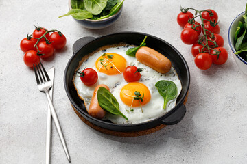 Two fried eggs in a small cast iron pan with tomatoes, spinach, sausages. English breakfast, keto diet.