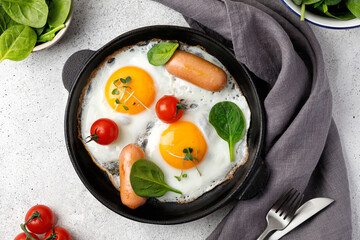 Breakfast with Fried eggs in a small pan with tomatoes, spinach, sausages, micro green. English...