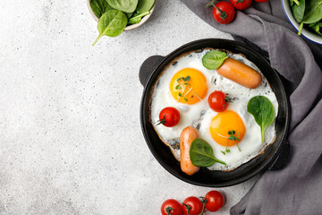 Fried eggs in a small pan with tomatoes, spinach, sausages. English breakfast, keto diet.