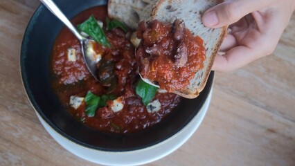 On the bread lay out a dish of healthy nutritious red beans prepared in tomato sauce with greens and with other ingredients. All ingredients are perfectly combined with each other. Mexican dish.
