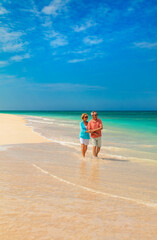 Retired couple in casual clothing walking on beach