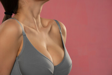 Large and beautiful women breasts in gray bra on pink background - obrazy, fototapety, plakaty