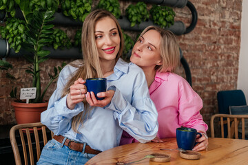 Two women friends sitting in cafe drinking coffee and laughing. Smiling caucasian girls chatting indoors