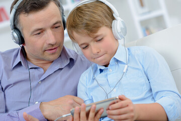 Man and boy wearing headphones, looking at electronic device