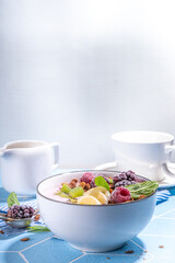 Summer breakfast healthy diet bowl with yogurt, granola, fresh fruit and berries, One portion with overnight fruity granola oats on sun-lighted tiled blue background copy space