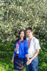 A young loving couple man and woman in embroidered shirts near a flowering tree in a spring garden.