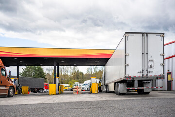 Truck driver refills the big rig semi truck tanks at the truck stop gas station to continue the cargo delivery
