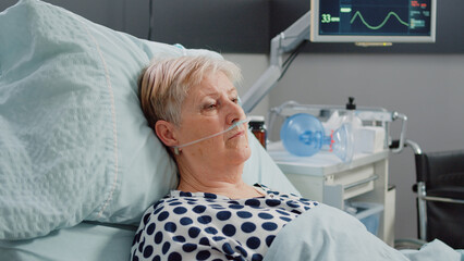 Portrait of retired woman with sickness laying in bed with heart rate monitor and oxygen tube for...