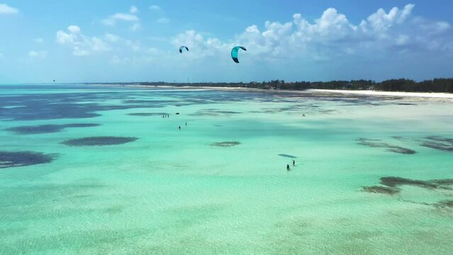 Rotating aerial view of people kitesurfing on a beautiful beach, a blue lagoon in Paje, Zanzibar, famous touristic destination for water sports