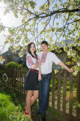 Fototapeta premium Young loving couple man and woman in white embroidered shirts near a flowering tree in a spring garden.