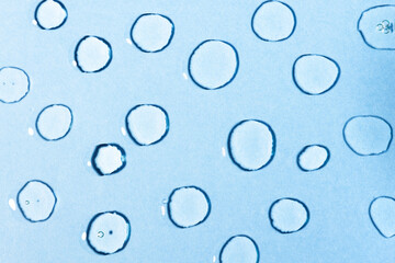 A lot of transparent cosmetic drops of liquid gel with bubbles on a blue background, top view. Moisturizing product for body skin, flat lay.