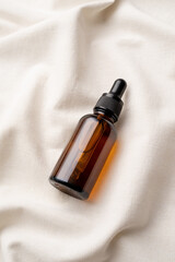 Fototapeta premium top view of amber glass essential oil droppper bottle with pipette on fabric wavy background