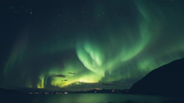 Aurora borealis above the fjord. Street lights and car lights flash in the background. Timelapse.
