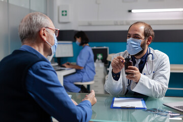 Fototapeta premium Elder person receiving bottle of pills from physician at consultation during covid 19 pandemic. Doctor with face mask giving prescription treatment in jar to patient at checkup visit.