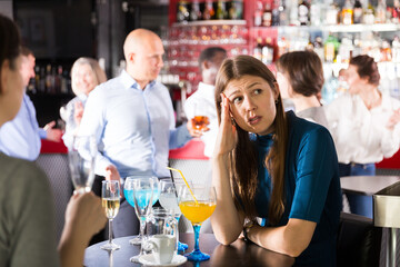 Bored woman sitting at table among dancing colleagues at corporate party
