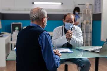Fototapeta premium Senior man meeting with general practitioner at checkup visit to do consultation and discuss about health care medicine during covid 19 pandemic. Medic and patient at examination.