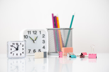 on the table there are two clocks of different sizes, a glass with colored pencils. there are a lot of colored stationery pins, two grinders and a gray pencil sharpener.