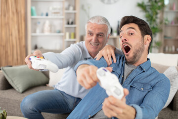 mature son and elderly father playing video game having fun