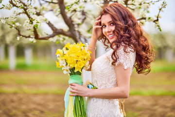 Portrait of a beautiful woman with long hair near flowering trees in spring.