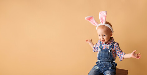 Cute little boy with bunny ears on beige background. Happy Easter