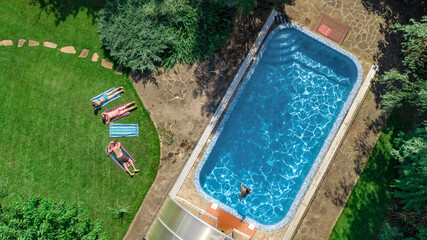 Happy family relaxing by swimming pool in summer garden, aerial drone view from above of parents and kids have fun on vacation, family weekend on resort
