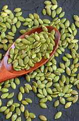 Peeled pumpkin seeds in a wooden spoon on a black background. Super food. Healthy food. Flat lay. Shelled pumpkin seeds. Vertical orientation
