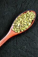 Peeled pumpkin seeds in a wooden spoon on a black background. Super food. Healthy food. Flat lay. Shelled pumpkin seeds. Vertical orientation