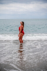 Woman in a bathing suit at the sea. A fat young woman in a red swimsuit enters the water during the surf