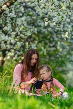 mother, with her daughter looking at the tablet on the background of flowering trees