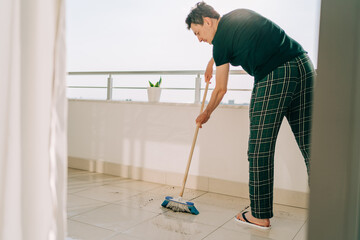 Man wiping floor with the mop. Janitor male washing the dirty floors. Guy mopping the balcony on a sunny day. Person doing home chores. Young fellow using cleaning equipment to dust the surface.