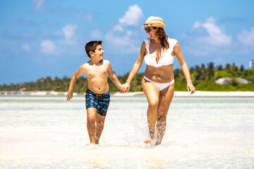 Fototapeta premium Mother and son running through the water on a white sand beach