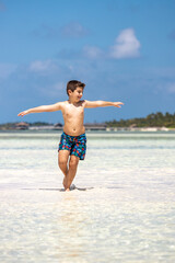 Funny kid running throw the water of a beach with open arms