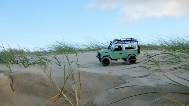 Small remote control jeep car toy drive on sandy dunes with coastal plants, static view