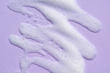 Foam swatch on a lilac background. Soapy liquid texture with bubbles. Natural sunshine and shadows....