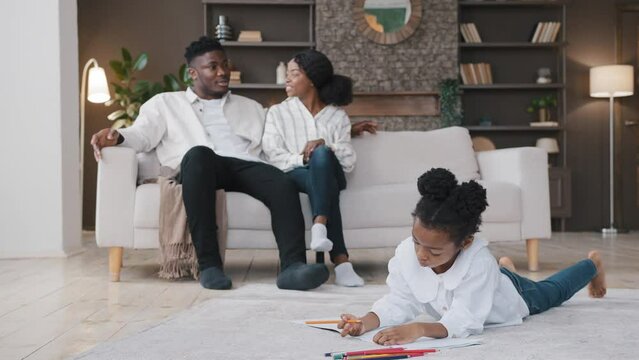 African family relaxing in new home rented flat own apartment. Parents casual talking sitting on couch in living room daughter drawing with color pencils lying on floor. Real estate insurance loan