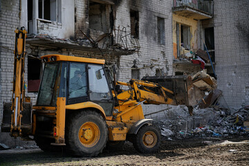 A tractor clears garbage near a destroyed town house. A large residential building without a window...