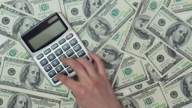 Woman's hand doing calculations on a calculator standing on money