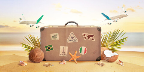 Retro suitcase on tropical beach surrounded by planes, palm leaves, coconuts and shells. Summer travel concept composition