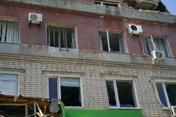The facade of the building with broken windows from the explosion of a shell in the war in Ukraine. Blinds flutter in the wind in broken windows