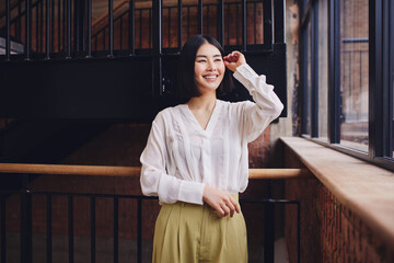 Portrait of cheerful mid adult Chinese businesswoman with hand in hair smiling and looking away