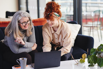 Portrait of two white businesswomen using laptop and smiling, senior woman with glasses and young...