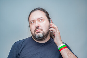 Obraz premium An unshaven man with bracelets in the colors of the Bulgarian flag listens attentively and incredulously to what they say on the phone.