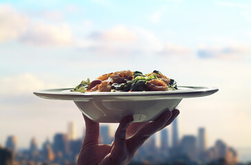 Waitress woman hand with plate of salad on skyscrapers of New York city background. View from roof...