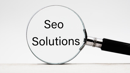 SEO SOLUTIONS text through a magnifying glass on a light background