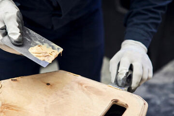 Putty of wood. Manual worker spackling wooden products at the carpentry manufacturing. Close up of...