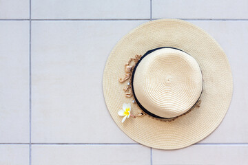 Summer beach straw hat with a necklace with shells and pearls and the plumeria flower on the tiled floor, top view.