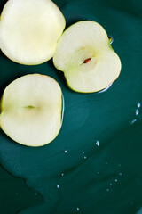 Top view of fresh sliced apples with juice or gel on green background, juice and gel serum, organic cosmetics, extract,  flat lay, copy space.