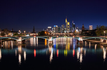 Fototapeta na wymiar Frankfurt skyline and illuminated Ignatz Bubis bridge reflecting in the Main river at night.